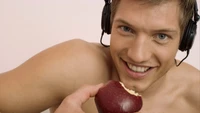 Hombre musculoso disfrutando de una manzana mientras escucha música