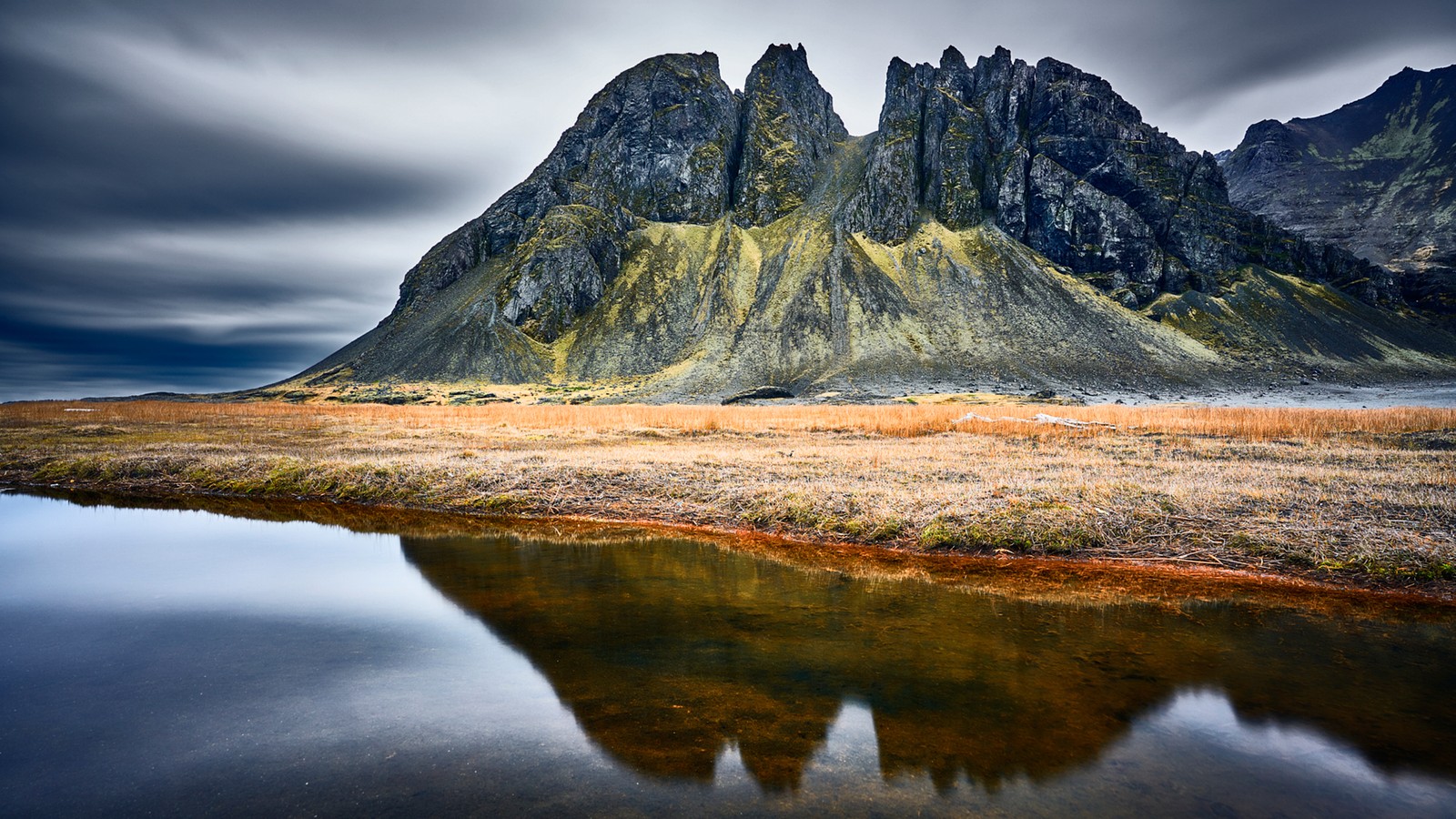 Uma montanha refletida em um pequeno lago no meio de um campo (montanhas, lago, reflexo, formas montanhosas, paisagem natural)