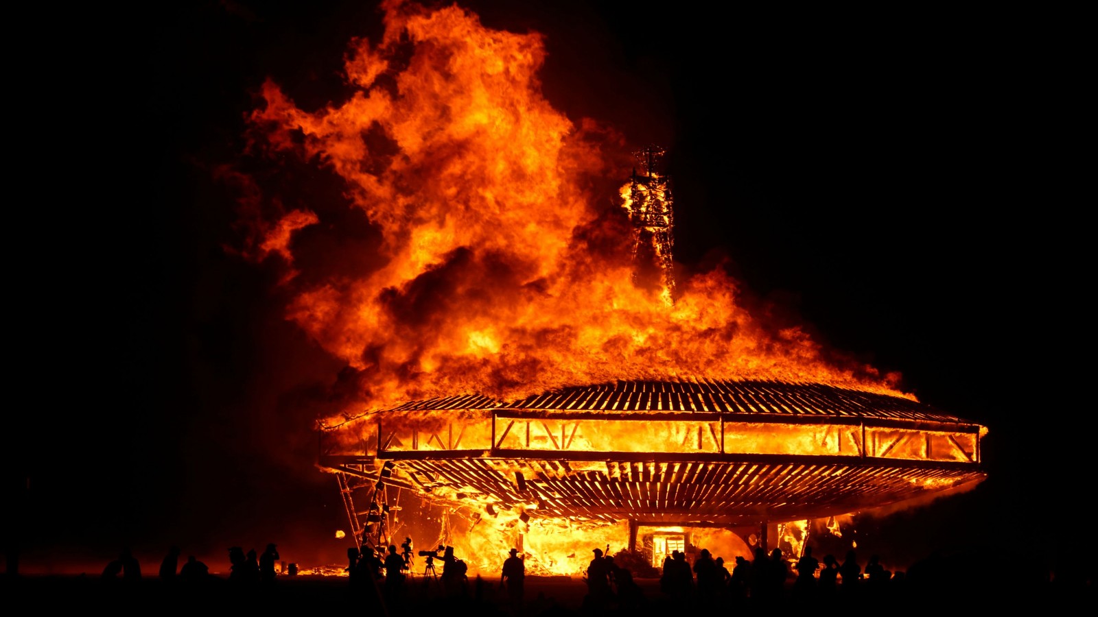 Un gran fuego ardiendo en la oscuridad con personas de pie alrededor (desierto de black rock, festival, fuego, calor, humo)