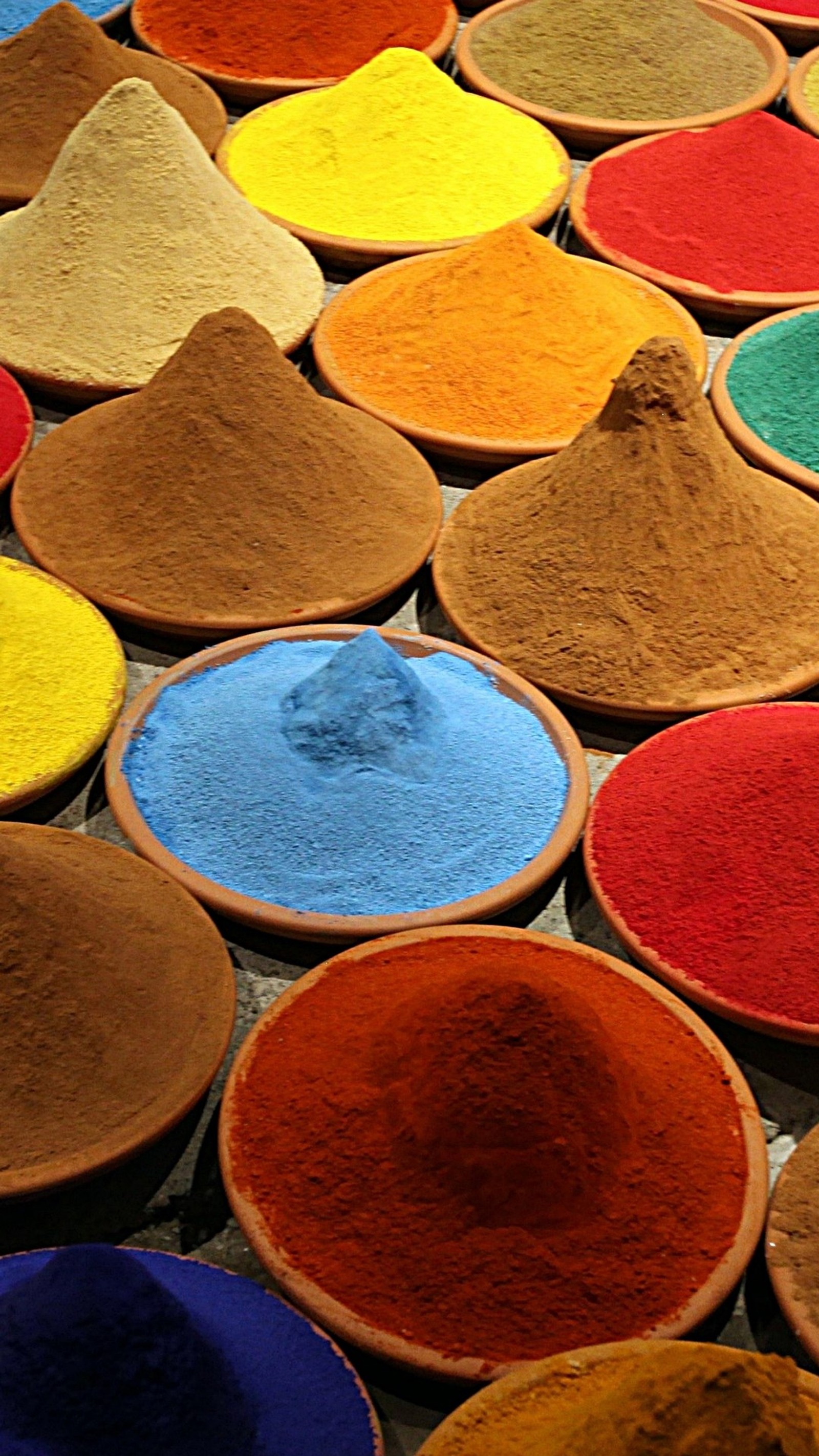 Arafed assortment of colorful powders in bowls on a table (colori, spezie)