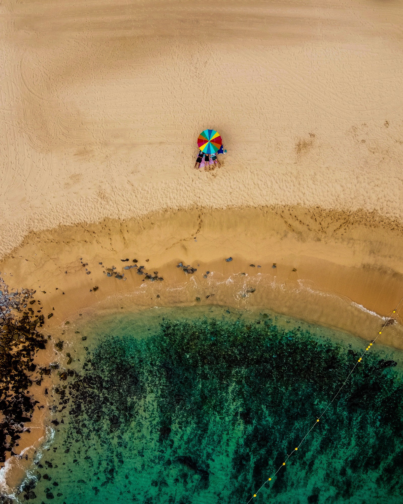 Vue aérienne d'une plage avec un parasol coloré et un corps d'eau bleu (sable, eau, écorégion, plage, art)