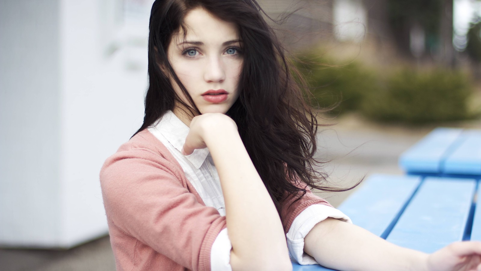 Hay una mujer sentada en un banco azul con la mano en su mentón (cabello, cabello castaño, color de ojos, pelo largo, peinado)