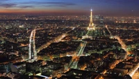 Una impresionante vista aérea de París al anochecer, con la iluminada Torre Eiffel y un vibrante paisaje urbano lleno de rascacielos y calles sinuosas.