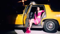 Tiffany Young, con un llamativo atuendo rosa, posa elegantemente junto a un taxi amarillo, exudando confianza y glamour.