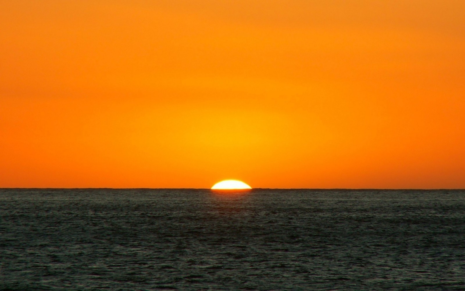 A close up of a sun setting over the ocean with a boat in the water (horizon, sunset, afterglow, sunrise, sea)