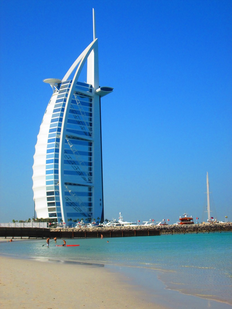 Арафед жирафы на пляже с лодкой в воде (бурдж аль араб, burj al arab, отель джумейра бич, jumeirah beach hotel, пляж джумейра)