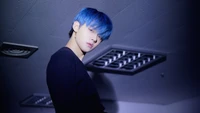 Yeonjun von TXT mit auffälligen blauen Haaren in einer schwach beleuchteten Umgebung.