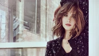 Dakota Johnson posando elegantemente ao lado de uma janela, exibindo seu cabelo castanho e seu traje estiloso.