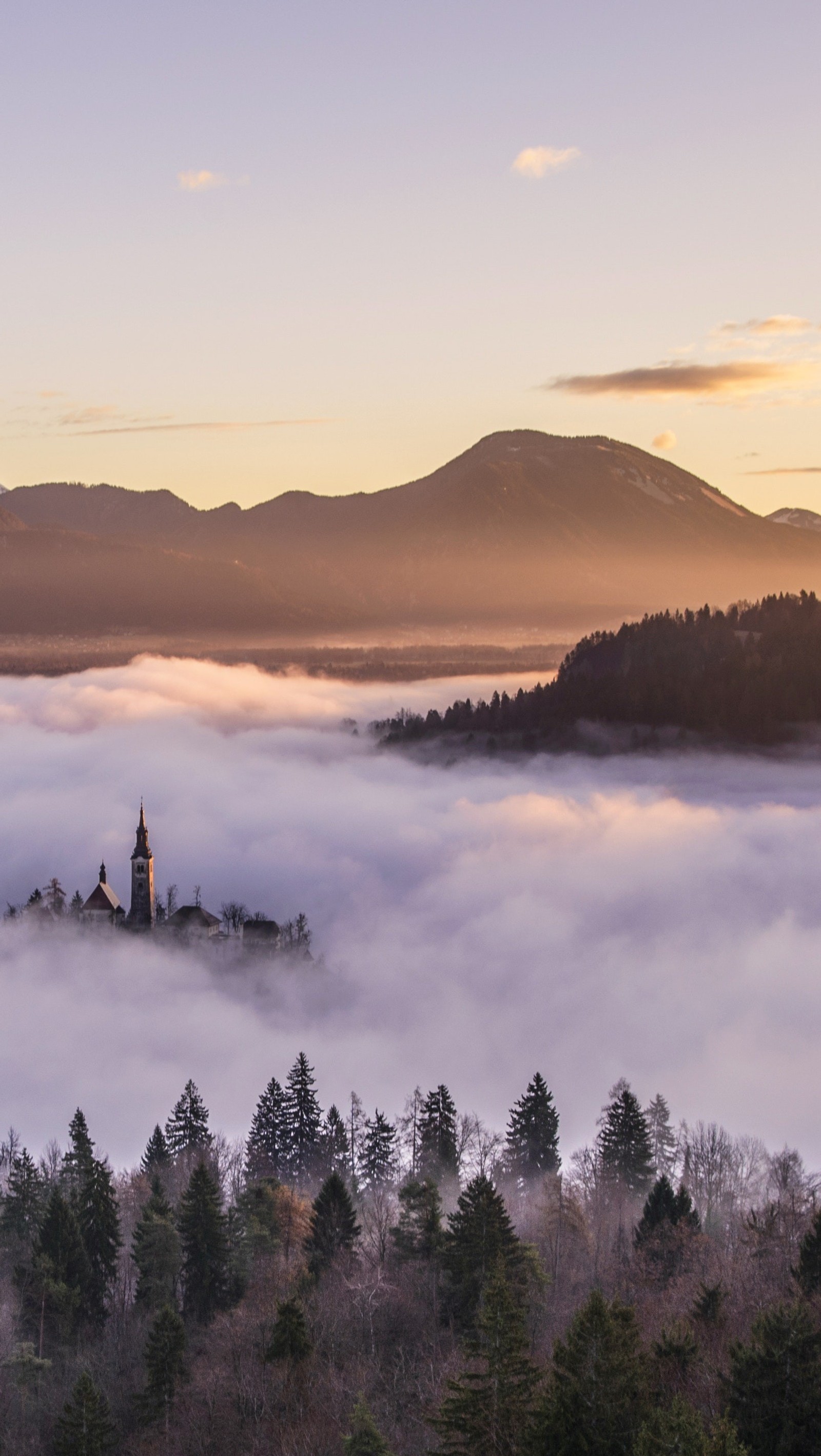 Montanhas cobertas de névoa e nuvens baixas com uma igreja ao longe (nuvem, montanha, atmosfera, ecorregião, água)