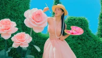 Seulgi de Red Velvet dans une robe rose pastel, peignant au milieu de grandes roses roses sur un fond bleu vibrant, incarnant un thème fantaisiste et artistique de "Feel My Rhythm".