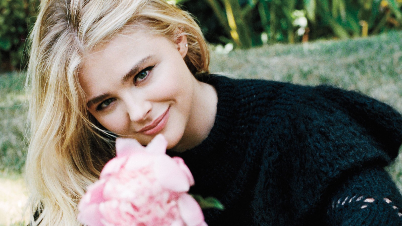 Une femme blonde avec une fleur rose dans la main posant pour une photo (chloë grace moretz, chloe grace moretz, célébrité, actrice, blonde)