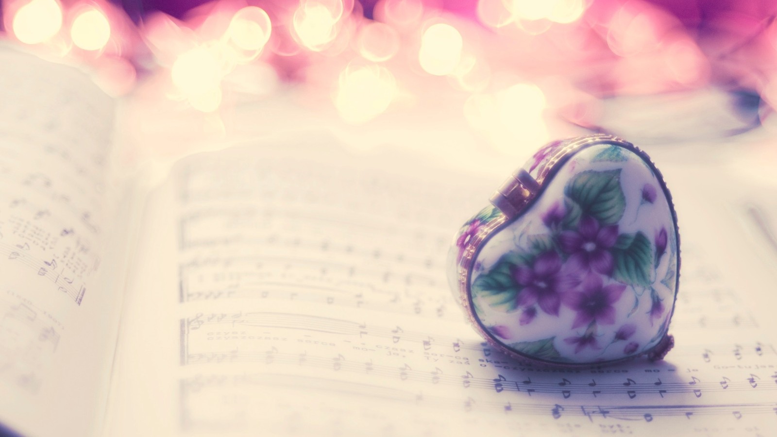 There is a heart shaped object on a book with music sheets (purple, violet, lilac, flower, playlist)