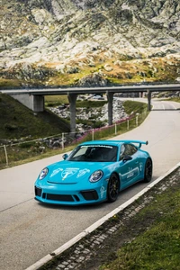 Porsche 911 GT3 em azul marcante, exibindo seu design elegante contra um cenário montanhoso em uma estrada sinuosa.