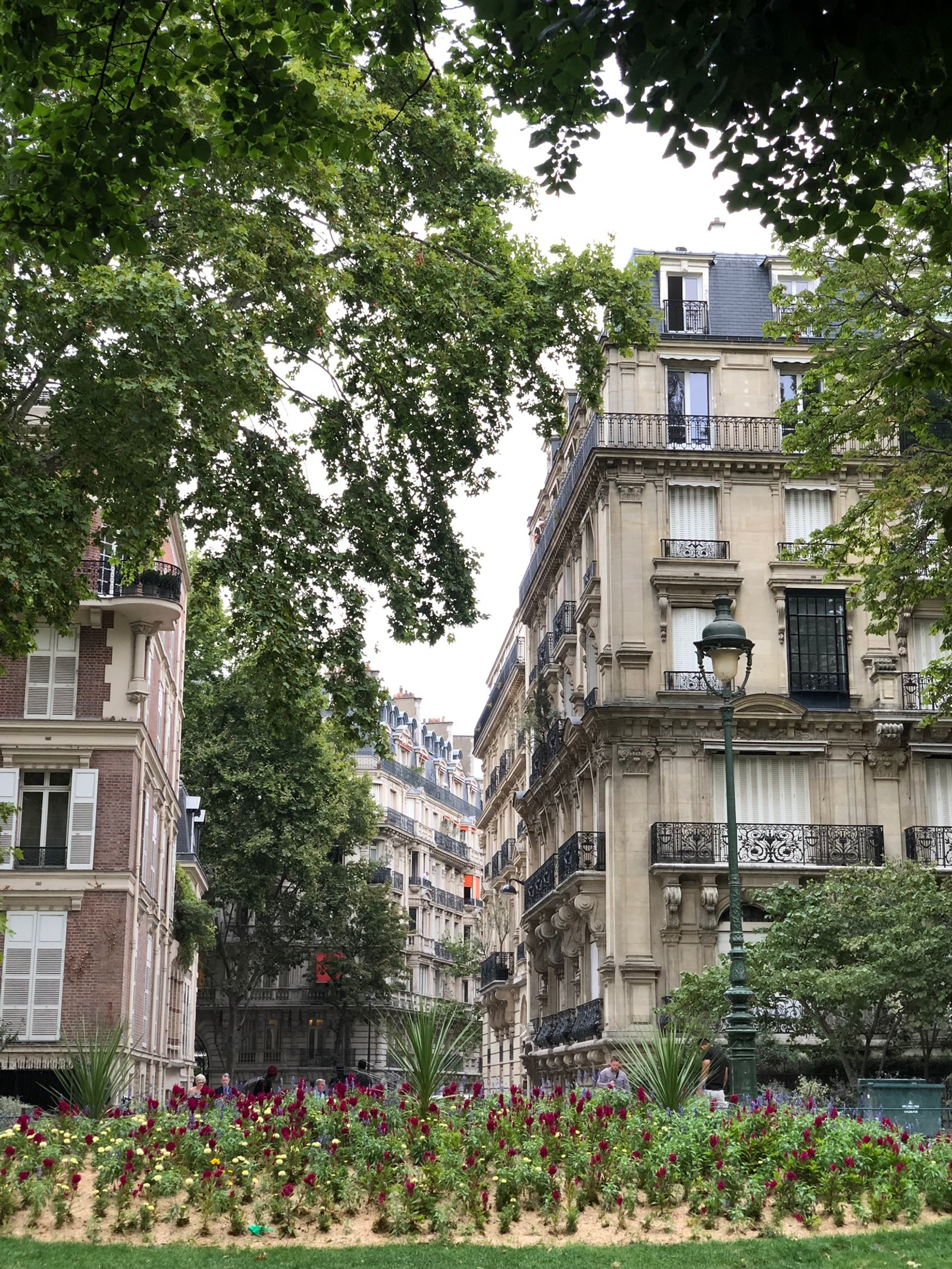 Há um parque com flores e árvores na frente de um prédio (paris, casa, jardim, imóveis, vizinhança)