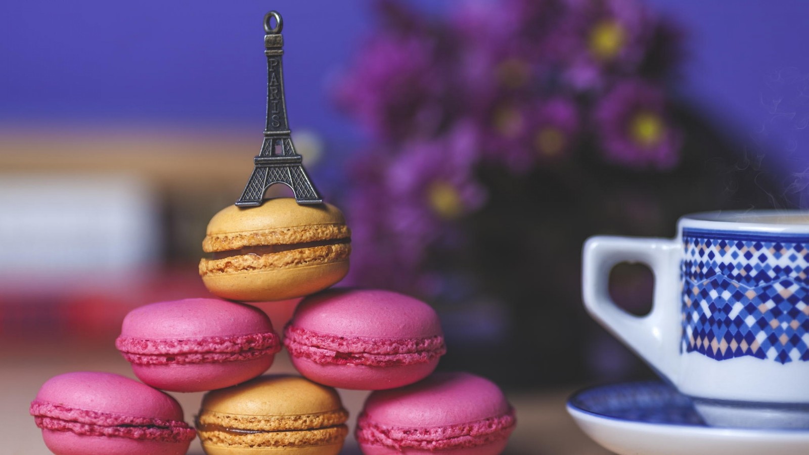 Il y a une tour de macarons sur une table à côté d'une tasse de café (macaron, tour, nourriture, douceur, tasse)