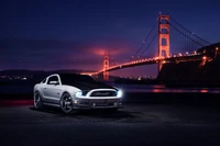 Sleek Shelby Mustang parked at night with the illuminated Golden Gate Bridge in the background.