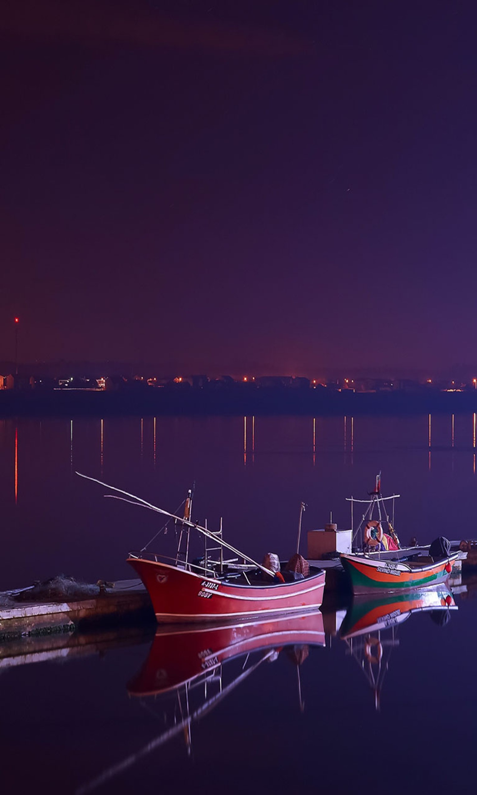 Barcos atracados na água à noite com uma cidade ao fundo (barcos, água)