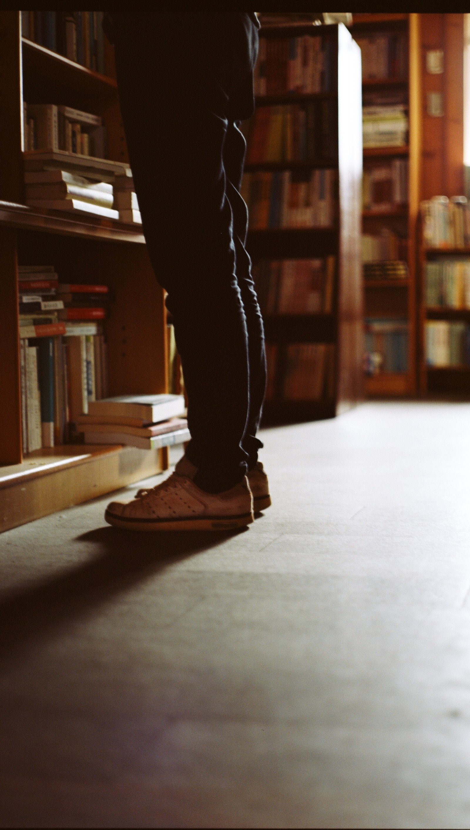 Une personne debout sur un skateboard dans une bibliothèque (jeans, bibliothèque, pantalon, chaussures)