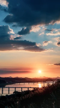 Pôr do sol sereno sobre a água com ponte e montanhas em silhueta