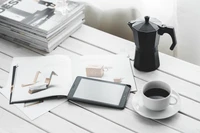 Configuration de café élégante avec une cafetière à moka, un smartphone élégant et une tasse de café noir sur un bureau minimaliste avec des magazines.