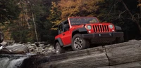 Jeep Wrangler rouge naviguant sur un terrain rocheux dans un paysage automnal pittoresque