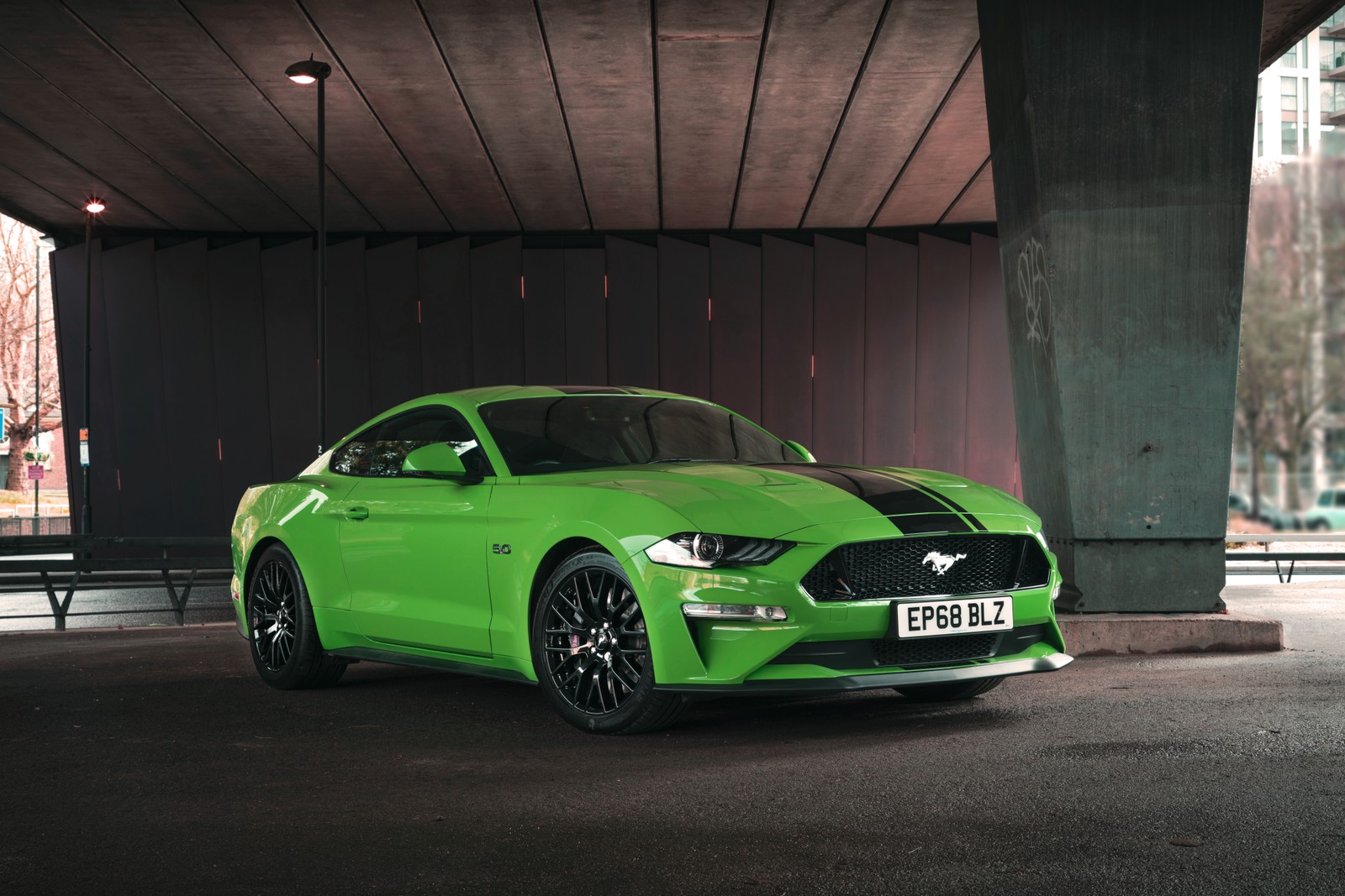 A green mustang parked in a parking lot under a bridge (shelby mustang, rim, ford, ford motor company, ford mustang)