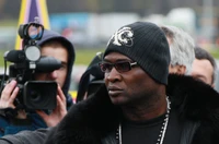 Stylish Individual in Sunglasses and Hat Surrounded by Media at a Boxing Event