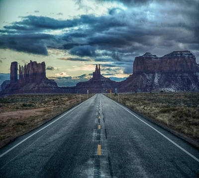 Una carretera escénica que conduce hacia formaciones rocosas dramáticas bajo un cielo melancólico en Arizona.