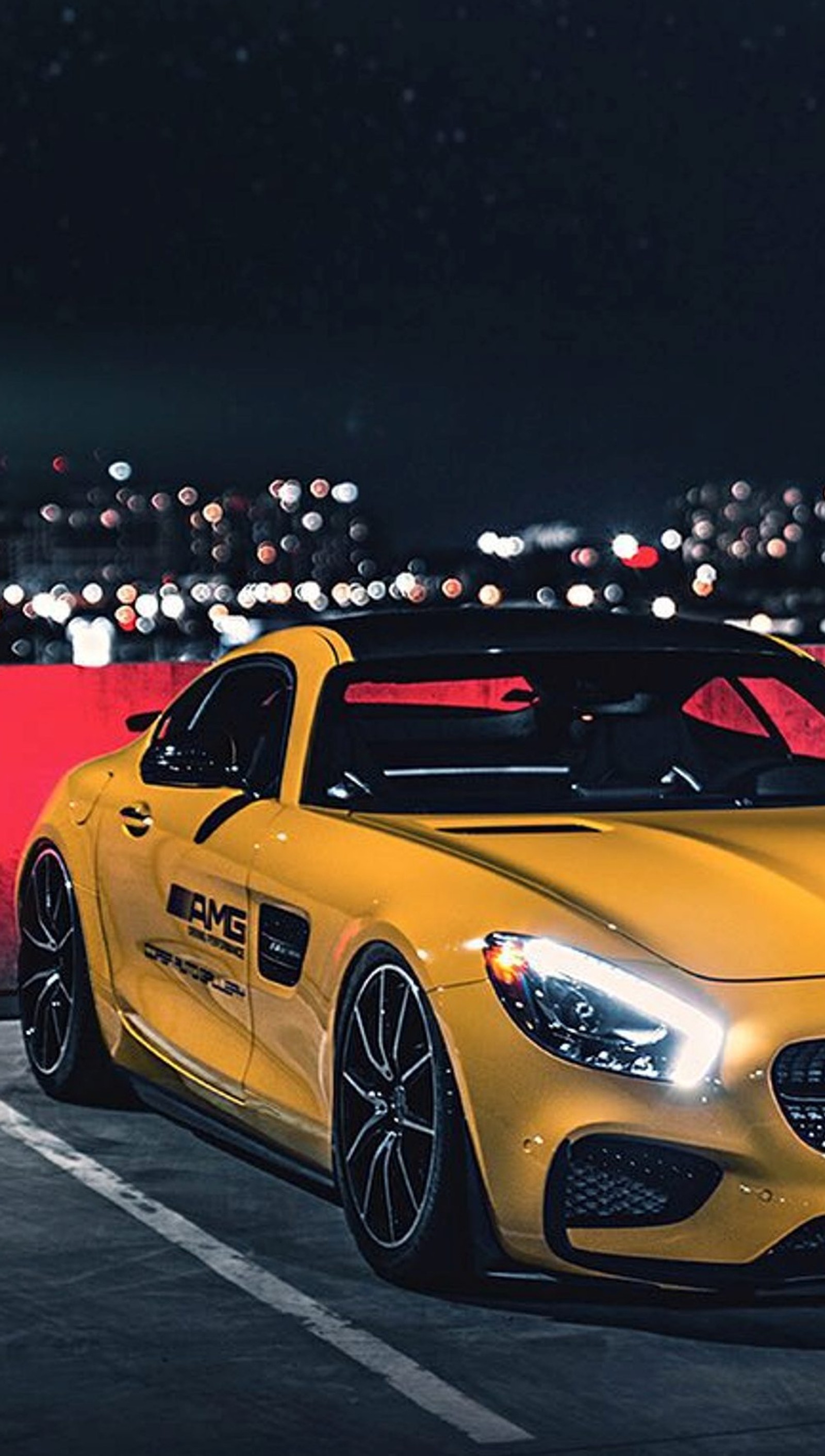 Um carro esportivo mercedes amarelo estacionado em um estacionamento à noite com luzes da cidade ao fundo (amg, carro, mercedes, amarelo)