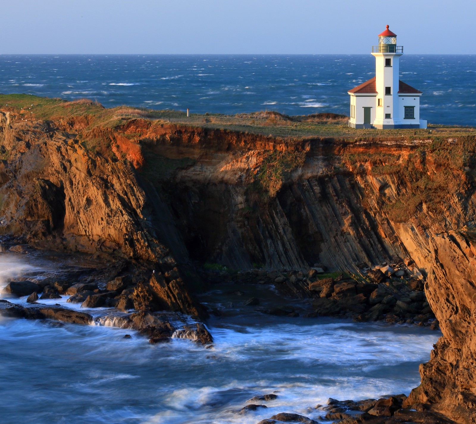 Um farol em um penhasco com vista para o oceano com ondas quebrando (praia, falésias, costa, rocha, mar)