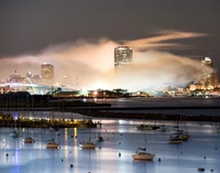 Paisagem urbana noturna com reflexos e névoa sobre o curso d'água