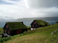 Charming black cottages with thatched roofs overlooking a serene fjord and lush highland terrain.