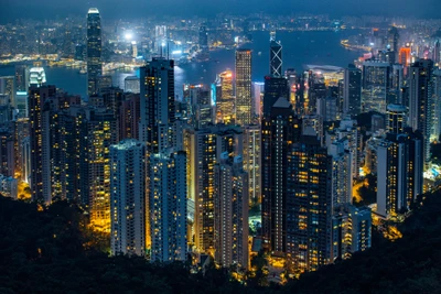 Vista aérea do vibrante horizonte de Hong Kong à noite, exibindo arranha-céus iluminados e luzes da cidade contra um impressionante fundo de porto.