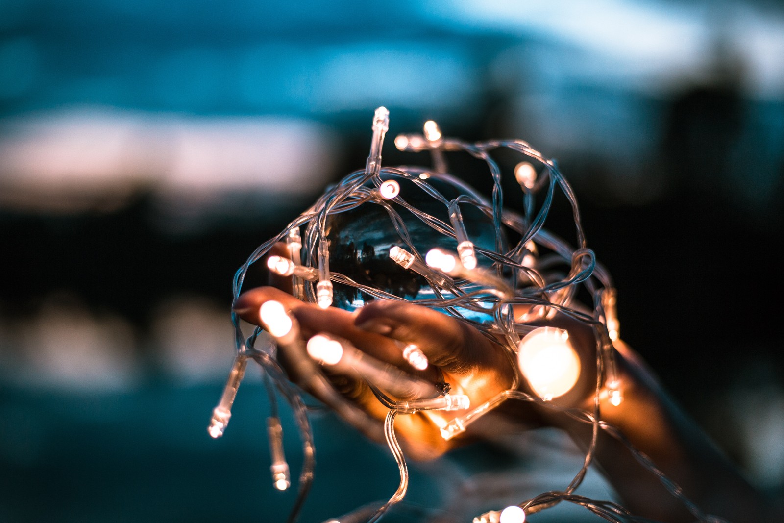 Jemand hält eine lichterkette in der hand mit einem verschwommenen hintergrund (licht, beleuchtung, glühbirne, blau, wasser)