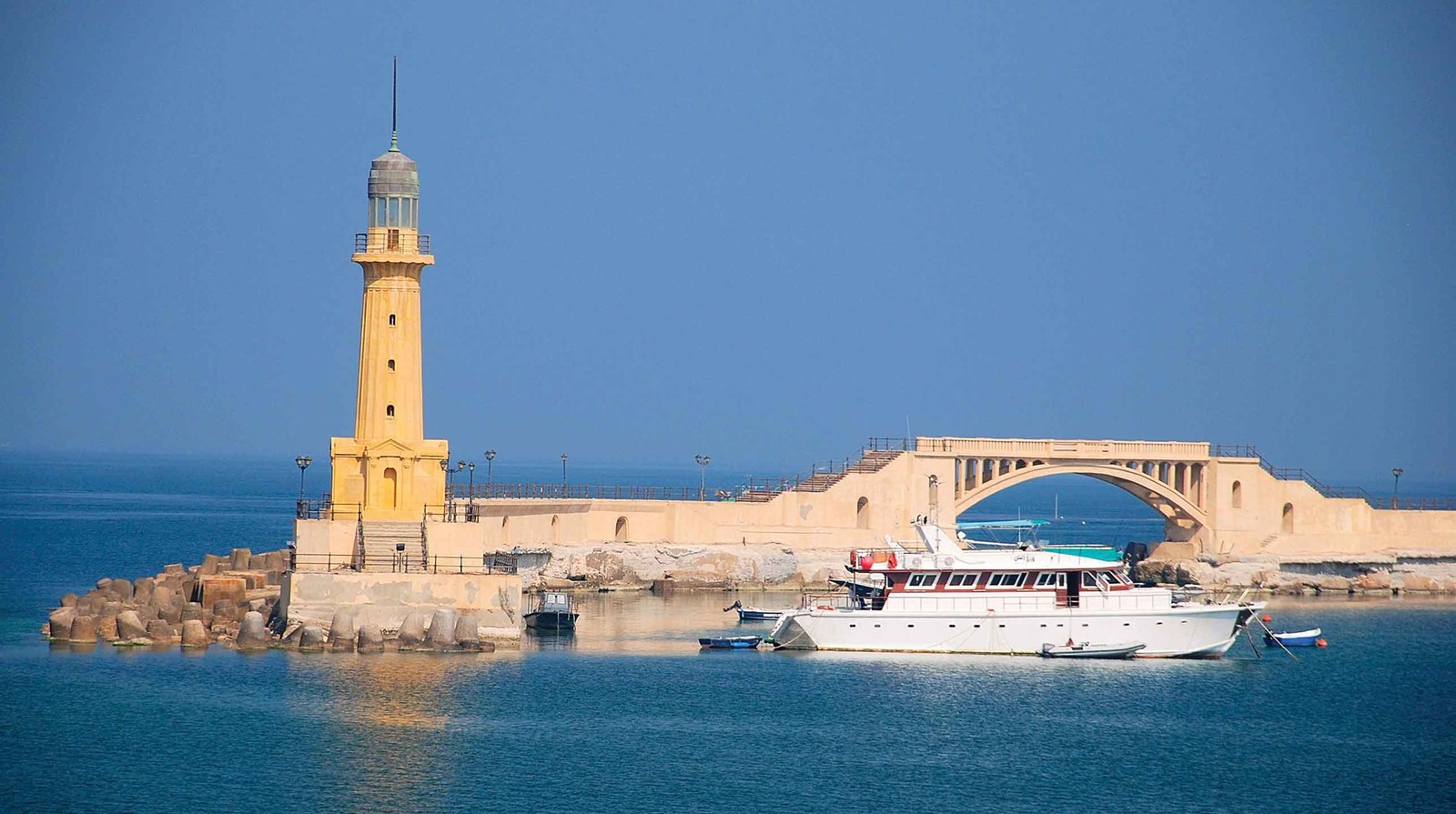 Arafed boat in the water near a light house and a bridge (tower, sea, tourism, lighthouse, tranquillity)