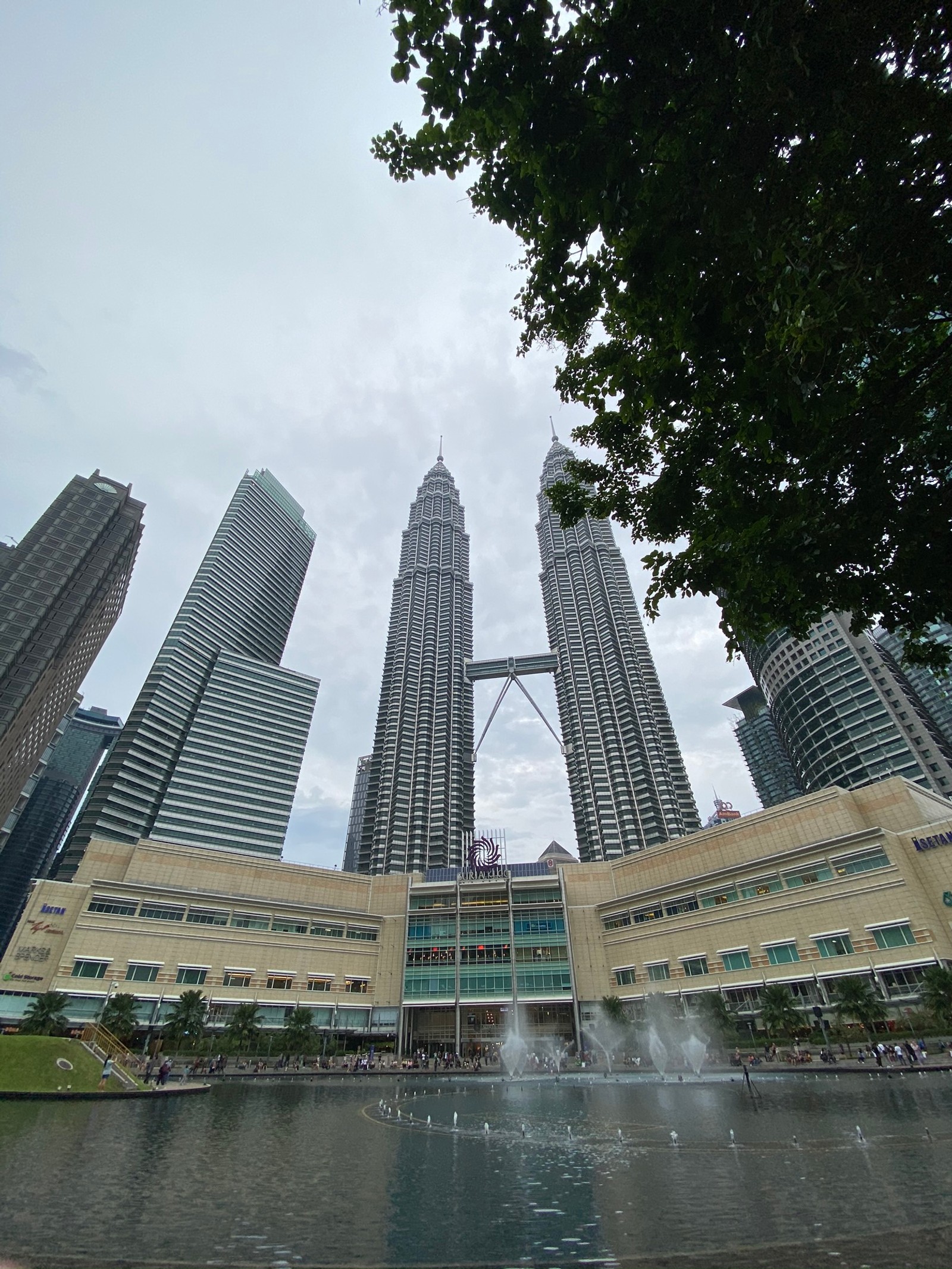 There is a fountain in front of a building with a fountain in front of it (petronas towers, kuala lumpur, water, tower block, daytime)