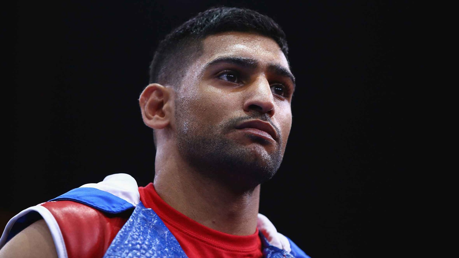 Un primer plano de un hombre con una camisa roja y un chaleco azul (boxeo, mentón, nariz, frente, vello facial)