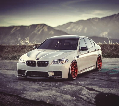 BMW F10 M5 modificado con llantas rojas llamativas, contra un fondo montañoso escénico.