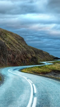 Winding Road Through Hills Under Dramatic Sky