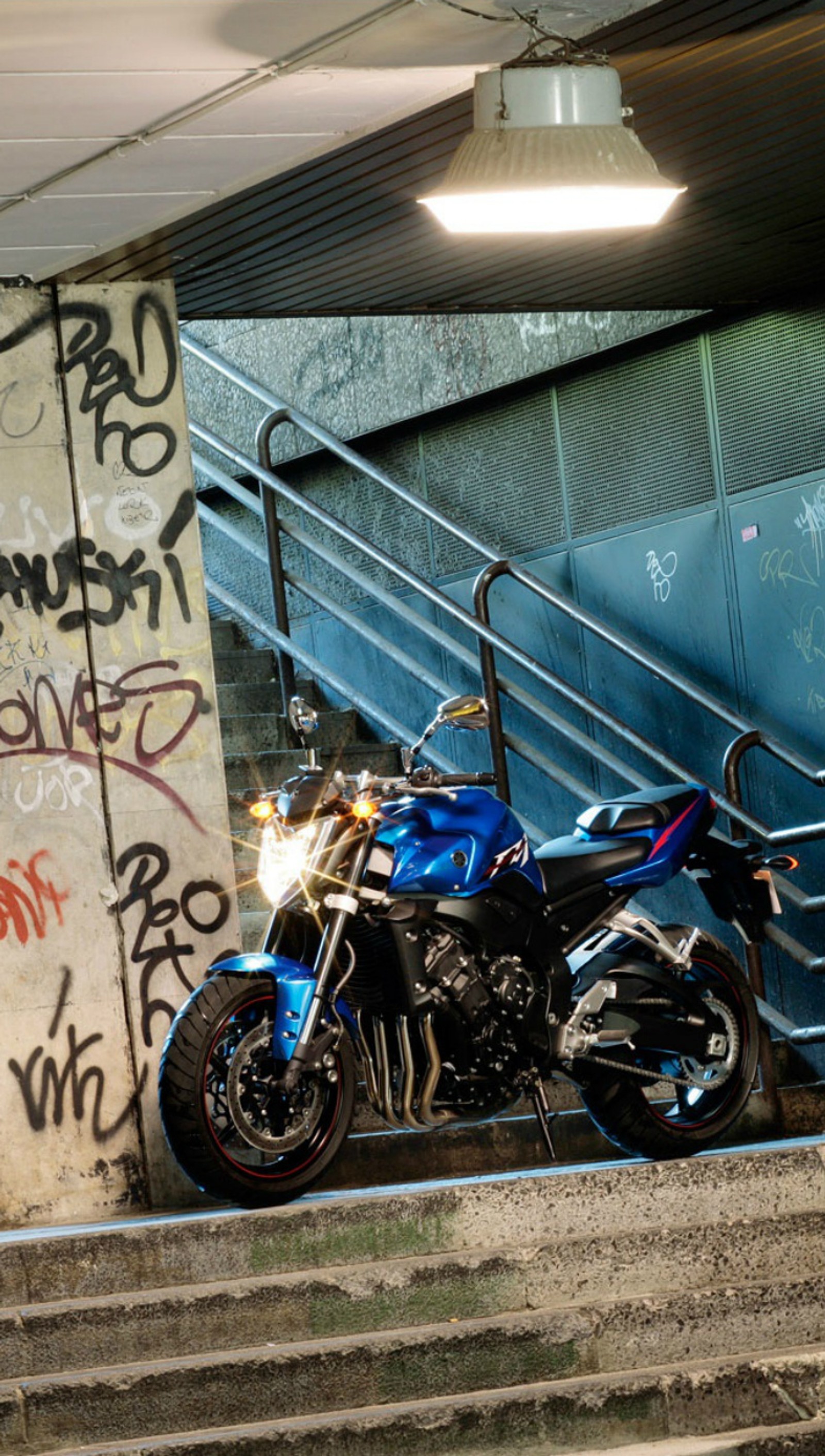 Hay una motocicleta estacionada junto a una pared con graffiti (moto, motocicleta, yamaha fz1)