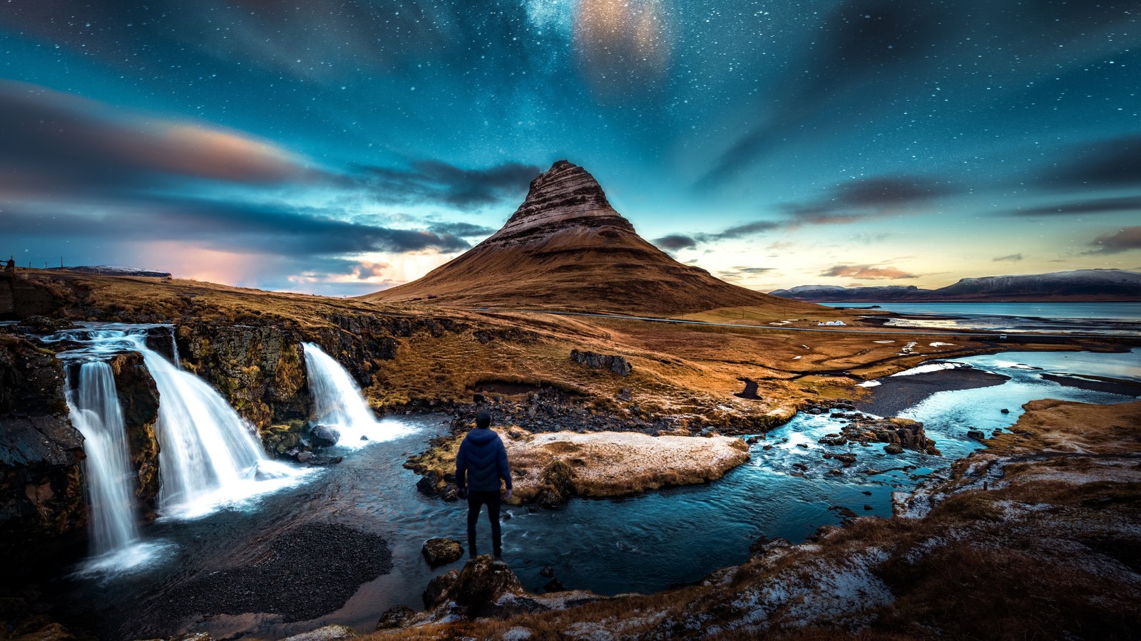 Un homme se tient sur un rocher regardant une cascade sous un ciel étoilé (étoiles, dusk mountains, paysage, nature)