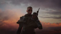 A lone outrider stands against a dramatic sunset, holding a communication device, poised for action in a gritty, sci-fi landscape.