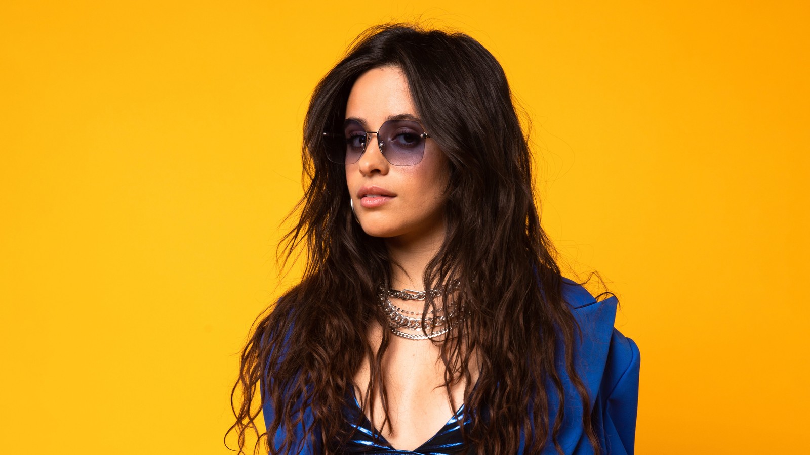 Une femme aux longs cheveux portant un top bleu et des lunettes de soleil (camila cabello, portrait, fond jaune, 5k, gens)