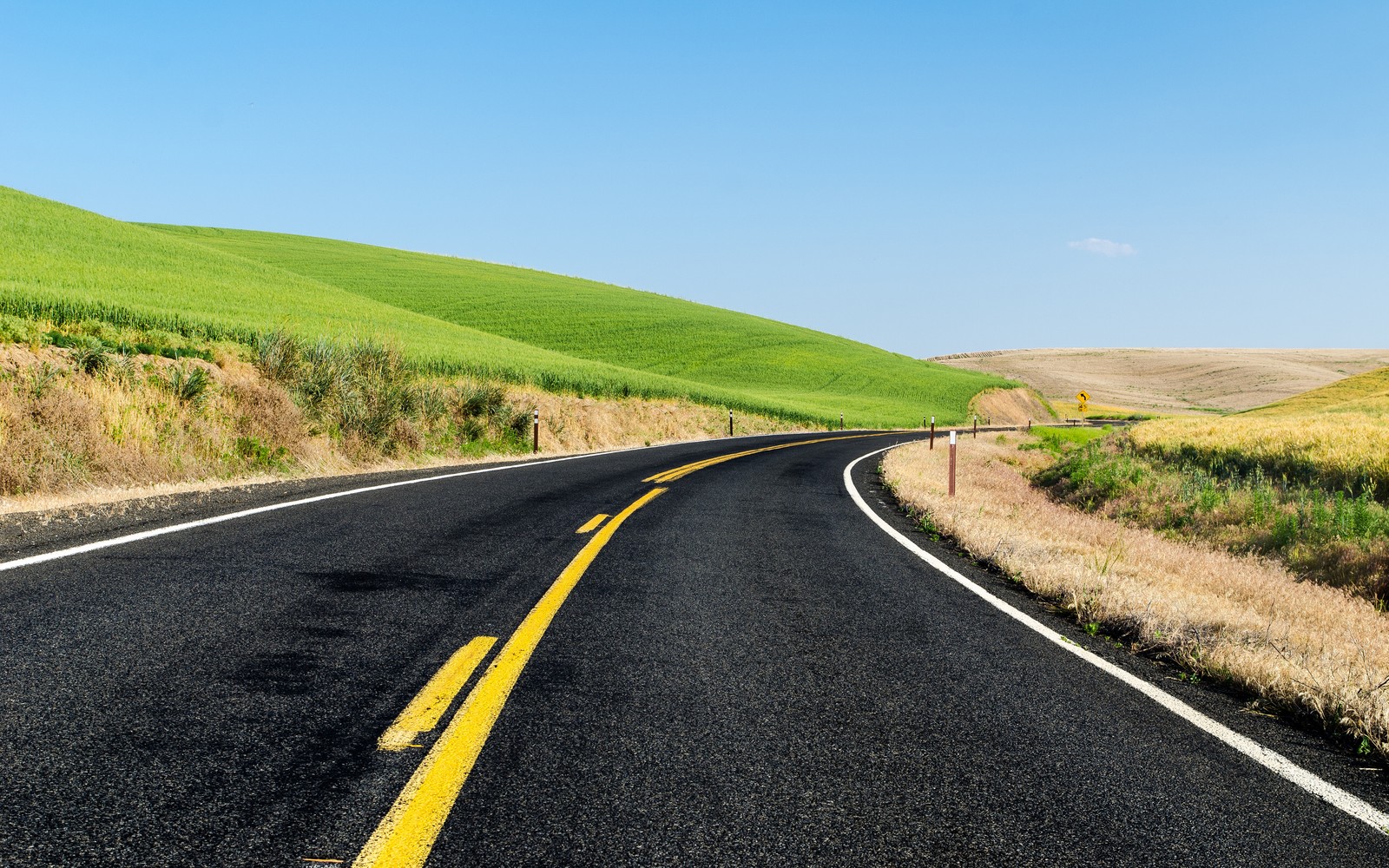 A view of a road with a yellow line going through a green field (green meadow, road, landscape, scenery, beautiful)