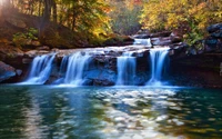 Ruhiger Wasserfall, der in einen ruhigen Pool fällt, umgeben von lebhaften herbstlichen Laub