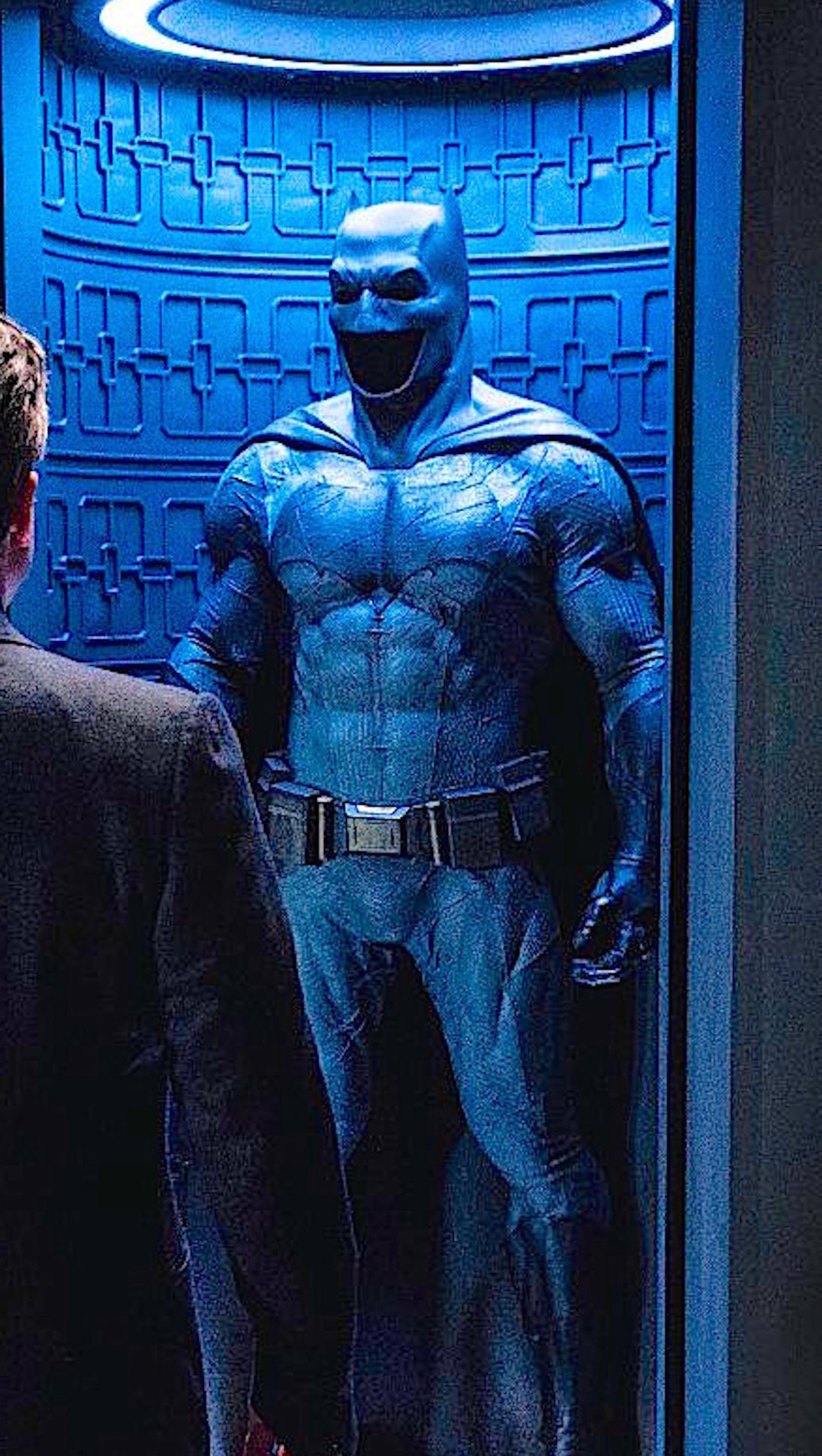 Disfraz de batman expuesto en una habitación azul con un hombre mirándolo (affleck, batman, batman v superman, el amanecer de la justicia)