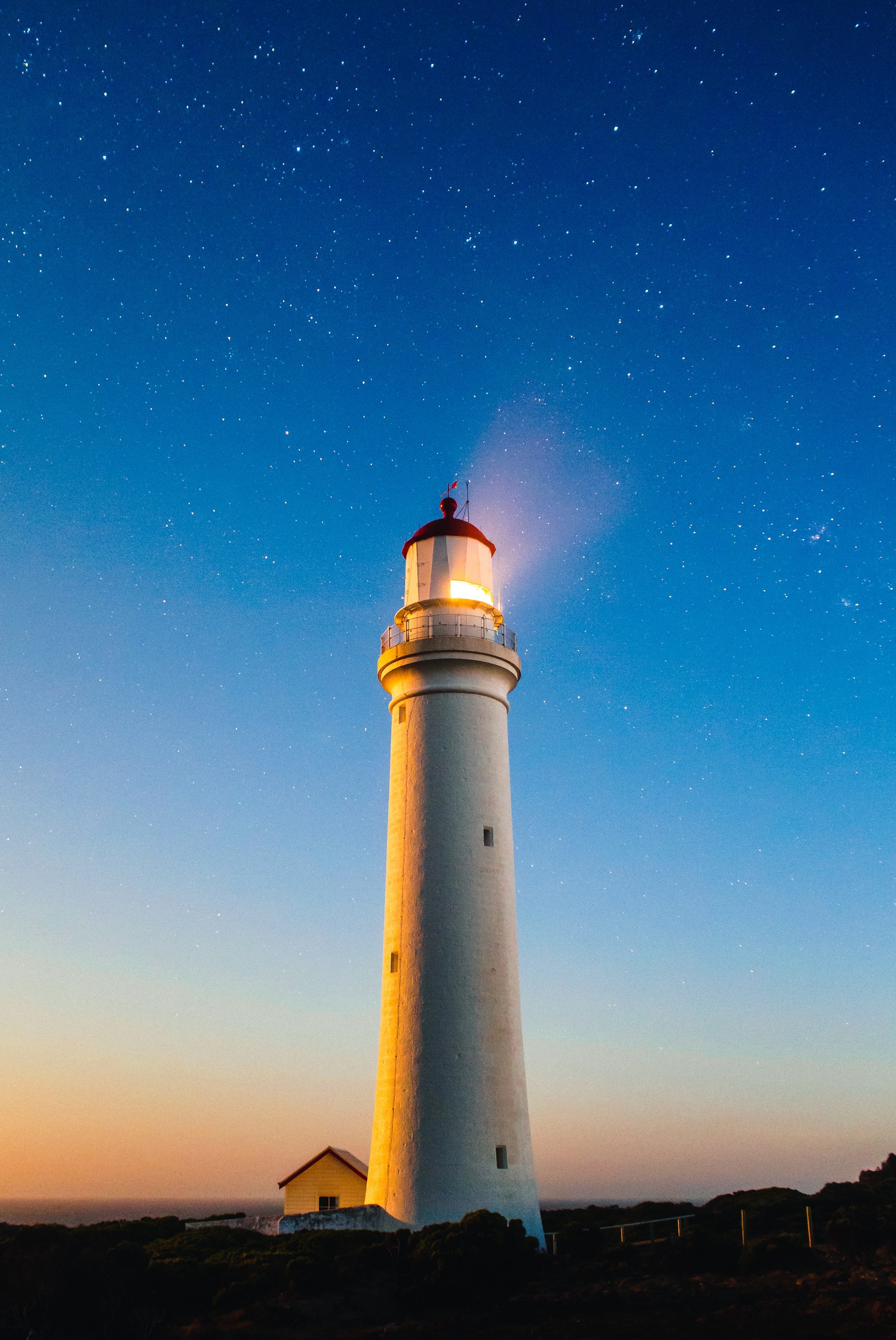 Há um farol com uma luz acesa no topo (costa, mar, farol, atmosfera, edifício)