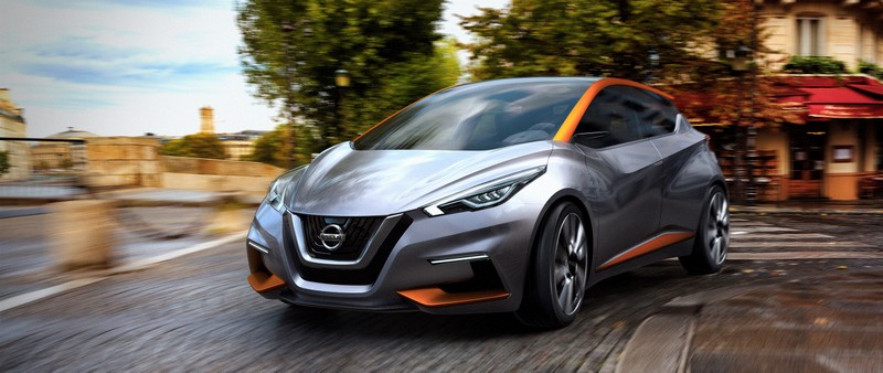 Серебристый nissan ur - v едет по улице перед зданием (машина, компактный автомобиль, семейный автомобиль, ниссан микра, nissan micra)