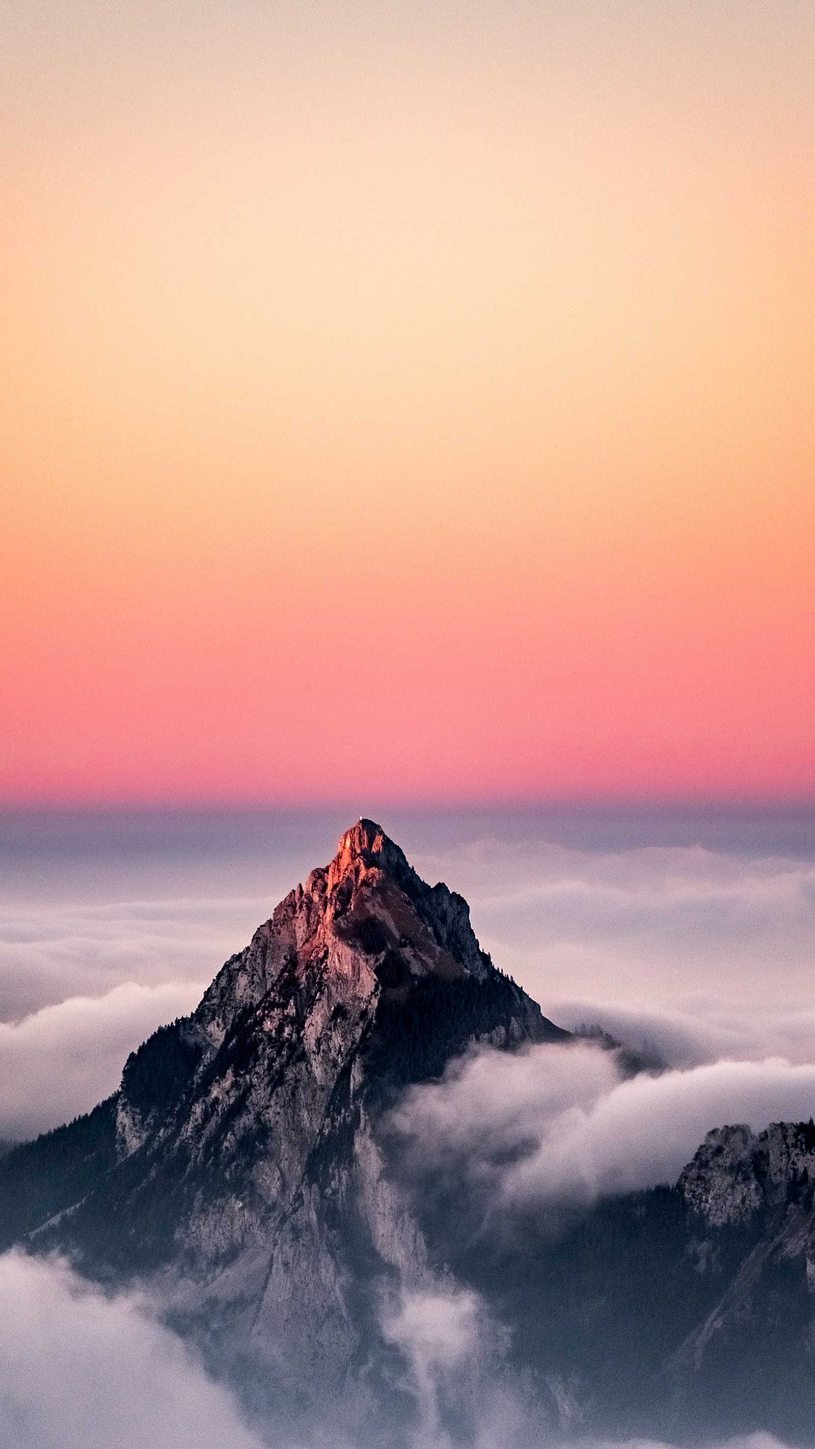 Arafed mountain with a pink sky and clouds below (mountain, atmosphere, cloud, afterglow, natural landscape)