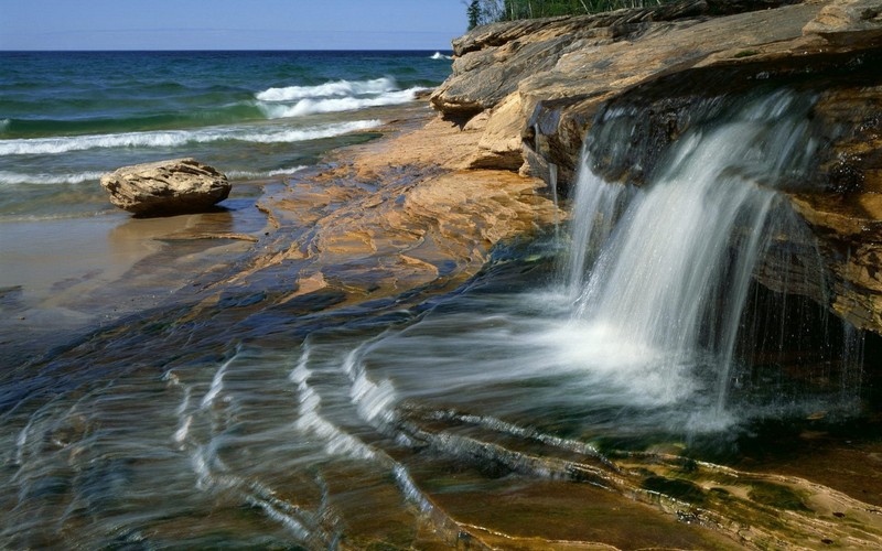 Крупный план водопада, стекающего на скалистый пляж (водоем, вода, скала, море, берег)